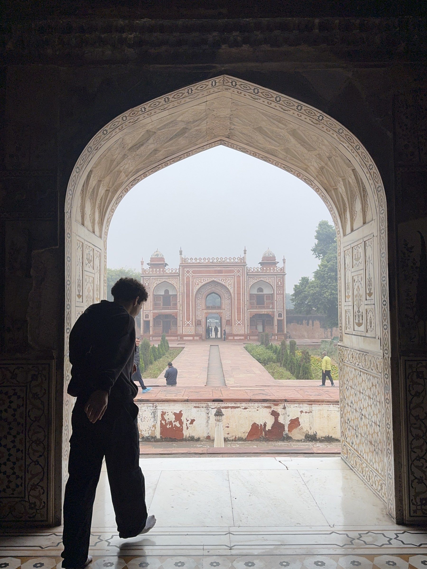 Silhouette of Orhun in a carved stone archway looking out at a red sandstone gate