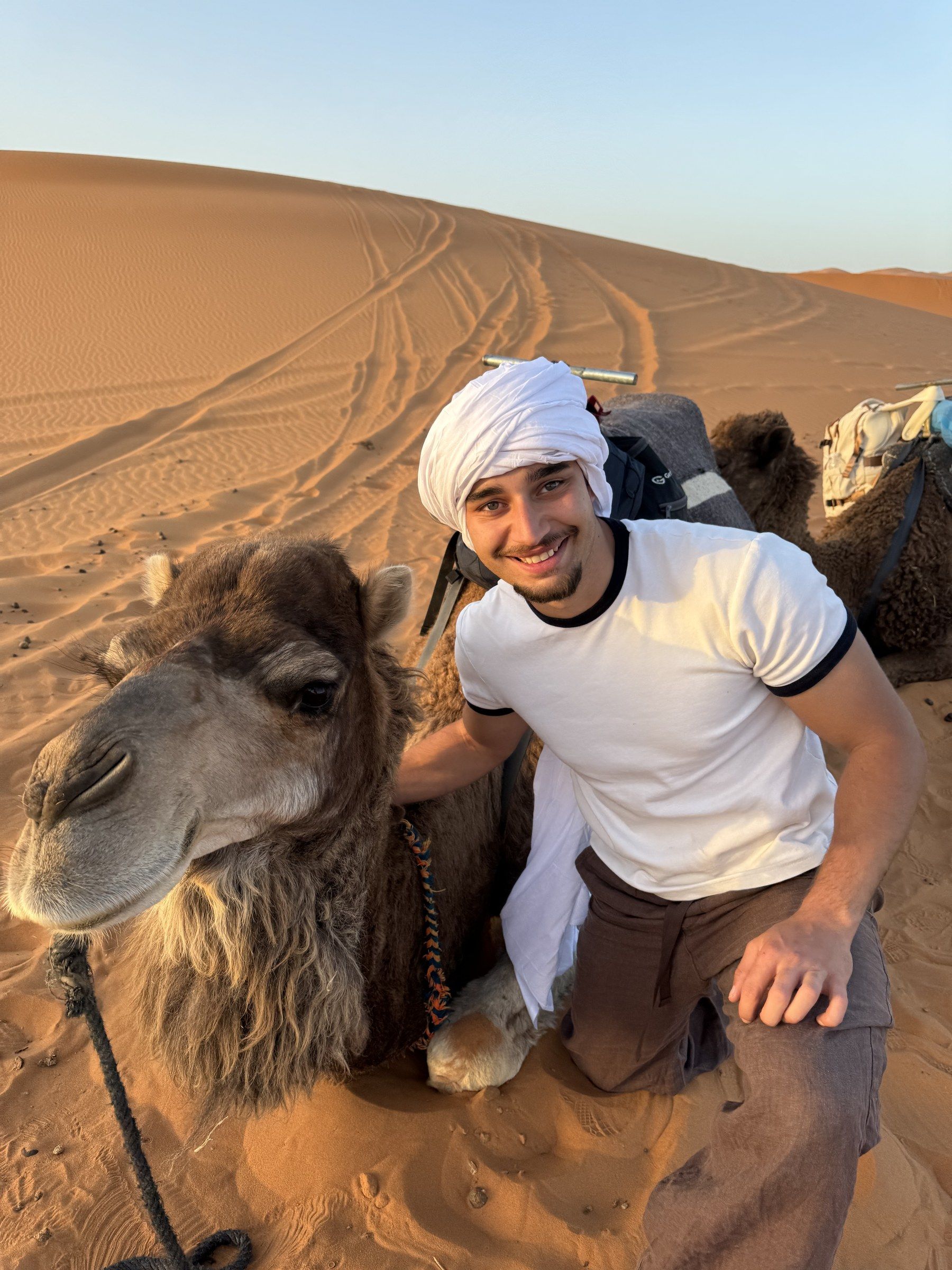 Orhun crouched next to a camel lying in the sand