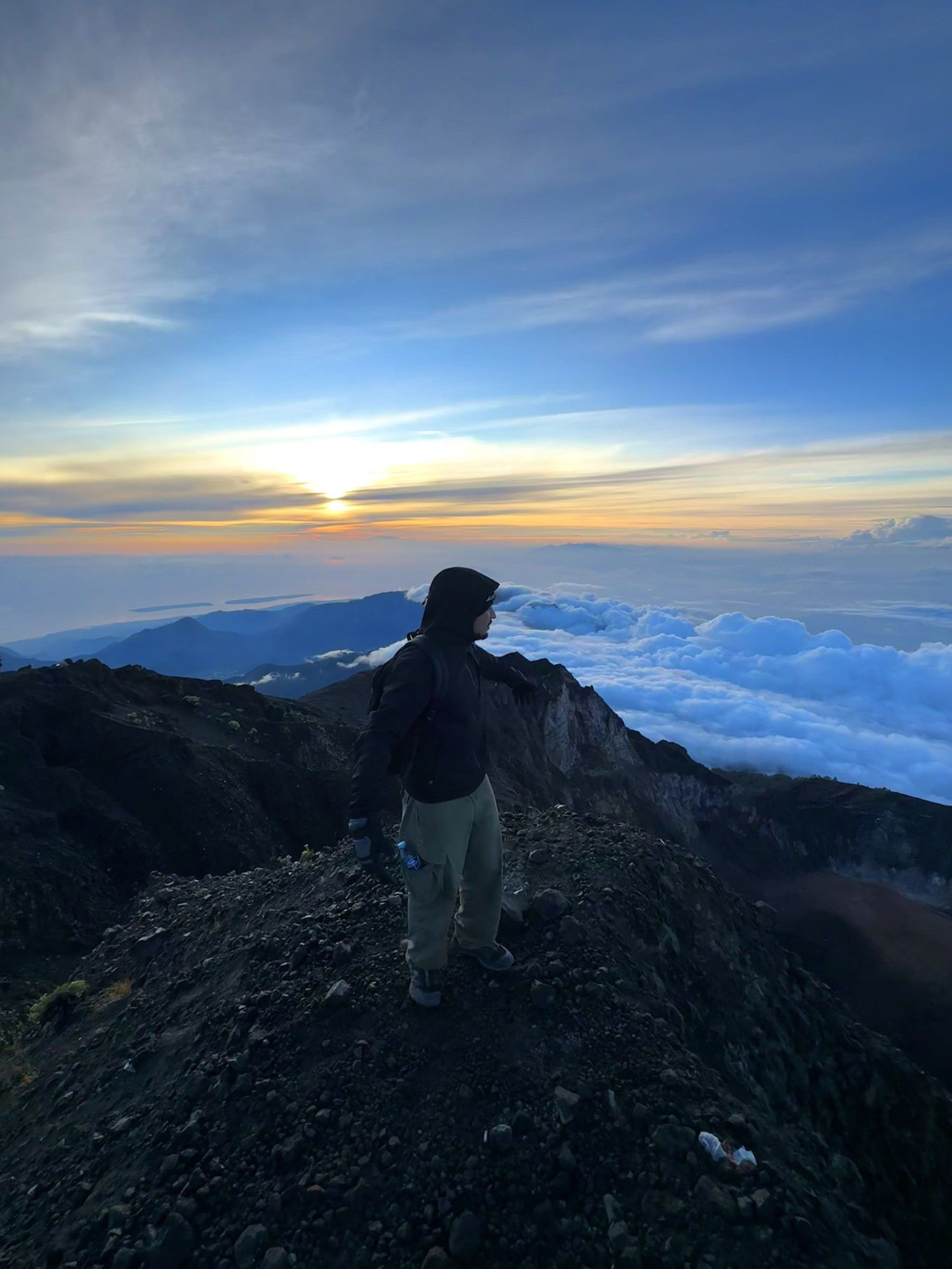 Orhun standing on a volcanic ridge above a sea of clouds at sunrise on Mount Rinjani