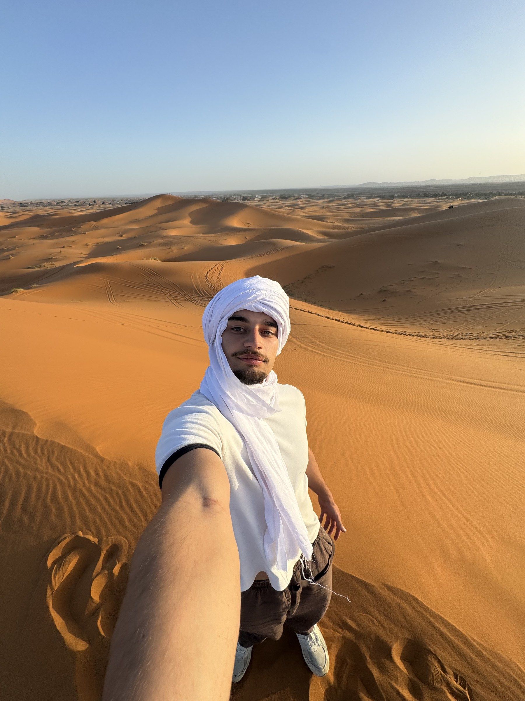 Selfie in a white head wrap on top of an orange Sahara dune