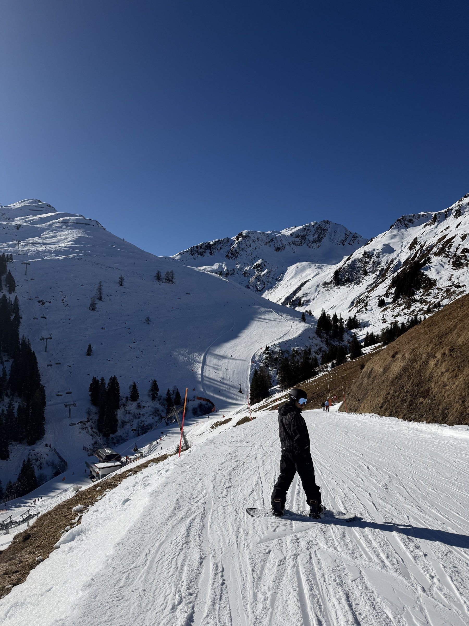 Orhun snowboarding down a sunny piste between snowy Alpine peaks